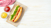 Homemade Hot Dog with mustard, ketchup, tomato and fresh salad leaves on white wooden background
