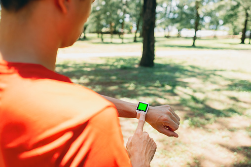 From a perspective behind the shoulder, a man carefully checks the data provided by the mobile app connected to his watch after exercising. He meticulously examines heart rate and other important indicators to ensure the effectiveness of his workout, such as cardiovascular endurance or calorie expenditure.Wearable technology. Healthy living lifestyle, sports routine concept