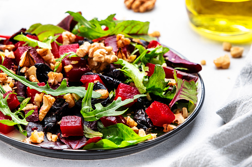 Healthy vegan salad with beetroot, prunes, arugula, chard and walnuts, white table background. Fresh useful vegetarian dish for clean eating