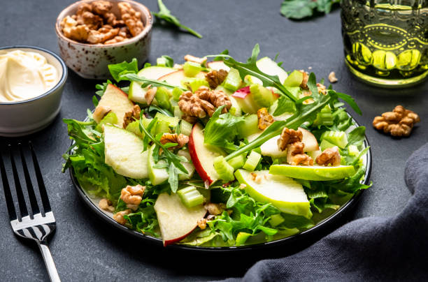 istock Waldorf salad with red and green apple, raw celery, lettuce, arugula and walnuts with mayonnaise dressing, black table background, top view 1500251904