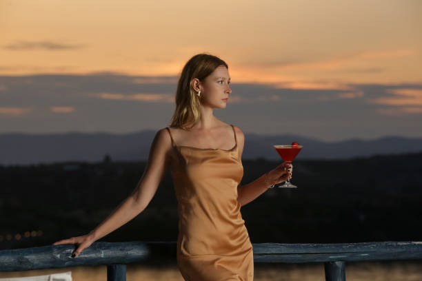 Fashionable young woman holding cocktail with beautiful sunset behind stock photo