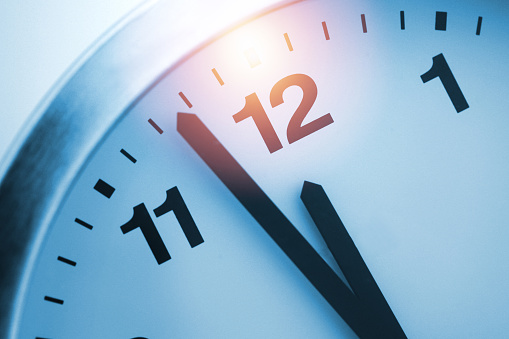 A Modern white wall clock with aluminium frame. Close up to a wall clock, the pointers at quarter pass 4. Selective focus on the number 5 or 5 o'clock. Reflections in the aluminum frame of the watch.