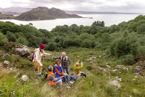 A small group of mature and senior friends sitting down and taking a break from their hike up the mountain landscape surrounding Loch Torridon in the Northwest Highlands, Scotland to sit, relax and chat while they enjoy eating their lunch.