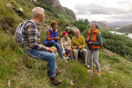 A small group of mature and senior friends sitting down and taking a break from their hike up the mountain landscape surrounding Loch Torridon in the Northwest Highlands, Scotland to sit, relax and chat while they enjoy eating their lunch.