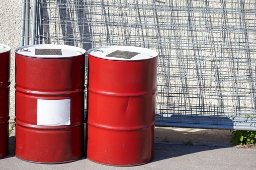 Two red barrels placed on the ground at a construction site with a metal grate in the background