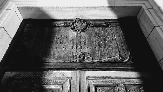 Old, mysterious  engraved wooden plaque above entrance to marble building.
