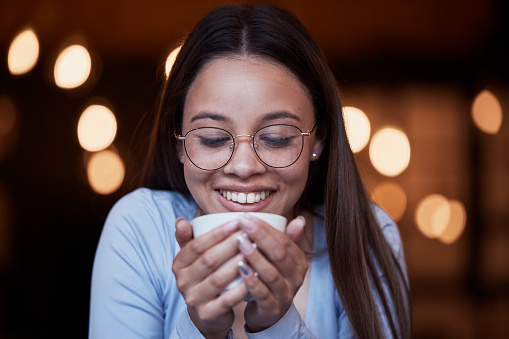 Smile, cup and a woman drinking coffee at night while working late in a dark office on a deadline. Happy, mug and an attractive young female smelling the aroma or scent from a fresh mug of caffeine
