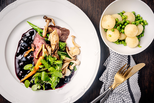 Overhead view of a dish of venison served with mushrooms, broccoli, carrots and new potatoes with a seasonal berry sauce and decorated with fresh pea shoots. Colour, horizontal format with some copy space. Photographed on location at a restaurant on the island of Moen in Denmark.