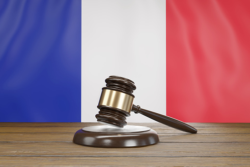 Small hammer gavel of judges of courts placed on a wooden table with the national flag of France as background. Illustration of the concept of French legal system and judicial issues