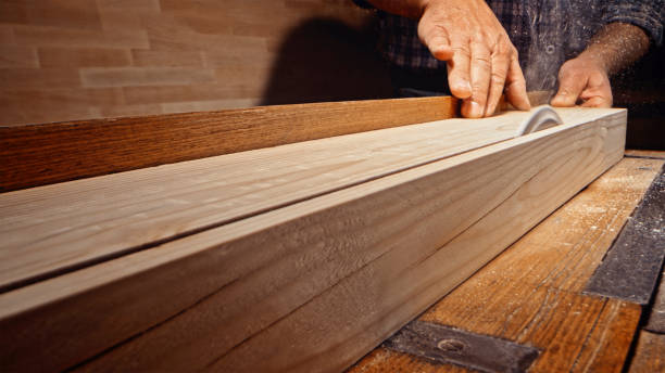 Close-up of male carpenter's hands cutting wooden plank with table saw in workshop.