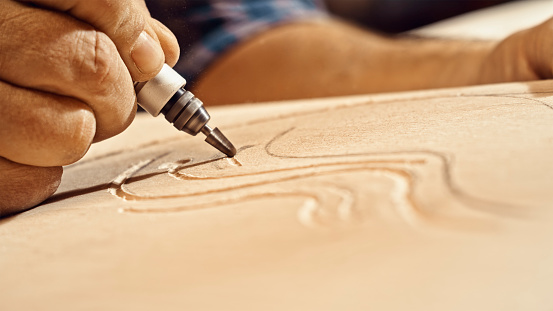 Close-up of male carpenter's hands carving on wooden plank in workshop.