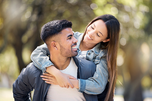 Couple, smile and outdoor on piggyback for love, care and happiness together in summer. Young man and woman at nature park for a moment on a happy and romantic date or vacation to relax