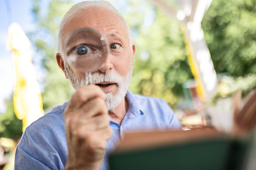 Elderly man with magnifying glass in hand reading book