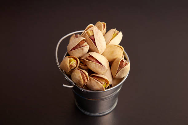 Pistachios in a small metal bucket on a black background.