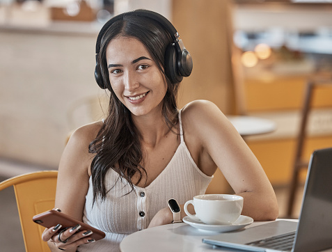 Headphones, phone and woman in cafe portrait listening to music, social media and mobile app chat for remote work. Young person on smartphone, audio technology and wifi for internet in coffee shop