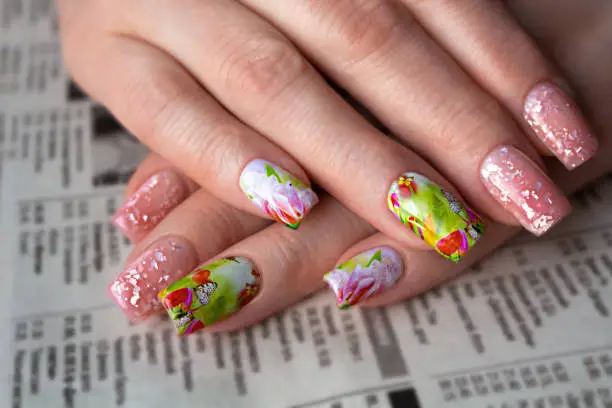 Photo of Light spring manicure with a sticker with a floral pattern and a gel polish with a shimmer on the background of a newaspaper for women 50+