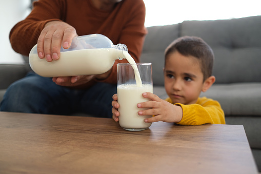 Man for son pours milk from jar into a glass cup