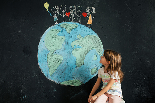 Little Girl looking at a Planet Earth chalk drawing on a blackboard wall that she draw