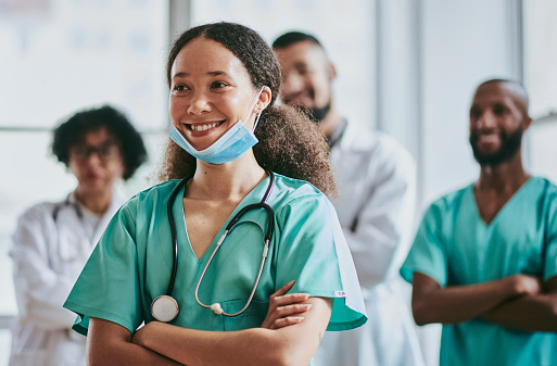 A young nurse stands with her hands crossed, smiling, while she briefs the patient about her medical procedure with three unrecognized doctors and a nurse in the background. Stock photo