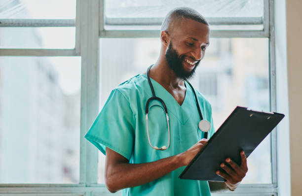 um jovem enfermeiro negro está de pé com um prontuário, escrevendo com espaço de cópia. foto de stock - male nurse medical student healthcare and medicine nursing assistant - fotografias e filmes do acervo