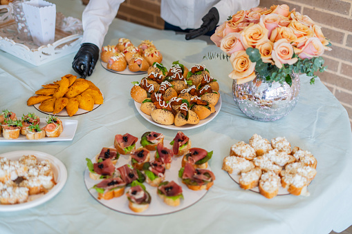 Average age 30-year-old Latina women dressed in white shirts and pants, professional waitresses are inside the facilities of a Veneto organizing the decoration and food table