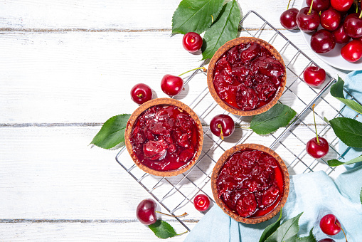 Cherry dessert tartlets. Mini tarts with cream filling and cherry topping, summer traditional pie, with fresh cherries on white wooden background