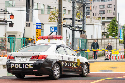 Tokyo, Japan - A police car on the street in front of a level crossing barrier in central Tokyo as pedestrians wait on the other side of the crossing.