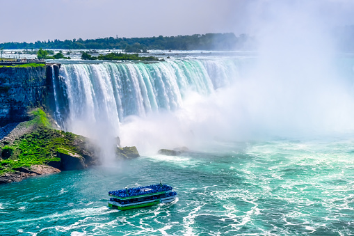 Niagara Falls, Canada - June 17, 2023: Small cruise ships full of tourists  in Niagara River. The international landmark is a major attraction