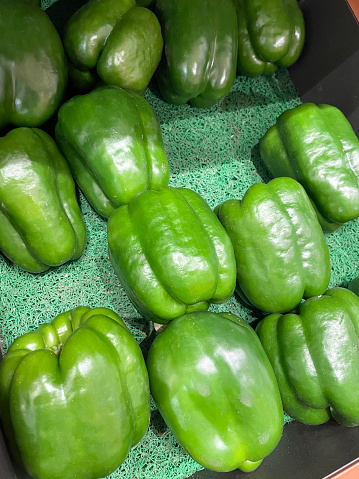 Stock photo showing a close-up view of green bell peppers (Capsicum annuum) being sold at an outdoor fruit and vegetable market.