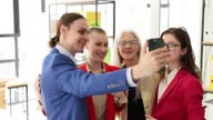istock Happy corporate team of company employees standing in modern office and looking at smartphone screen, taking selfie 1500312222