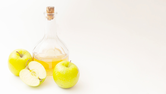 A decanter with apple cider vinegar, two and half apples on white background, copyspace