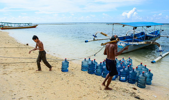 Bali, Indonesia - Apr 17, 2016. Local men loading goods on sand beach at summer day in Bali Island, Indonesia.