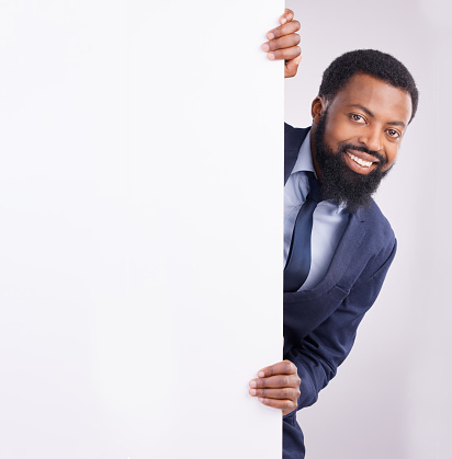 Hiding, portrait and a black man standing by a wall isolated on a white background in a studio. Mockup, happy and an African corporate employee looking from a corner with space for advertising