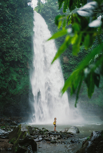 Cheerful woman standing near the  refreshing waterfall on Bali, Indonesia