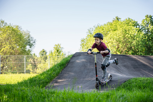 Boy riding push scooter at the pump track at sunset