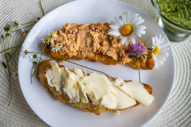 2 piece of croissant with butter and tuna spread on white plate, flowers, closeup. stock photo