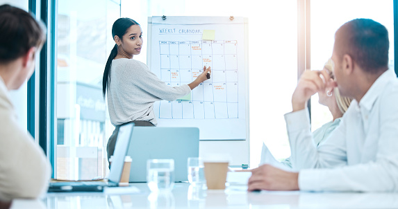 Business people, coaching and meeting on whiteboard for schedule planning with calendar for daily tasks at office. Female coach training staff for team reminder or weekly planner in conference room