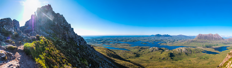 Panoramic vista across the remote mountain wilderness of Inverpolly, past the blue loch waters to the iconic peaks of Cut Mor to Suilven beyond, deep in the Highlands of Scotland.
