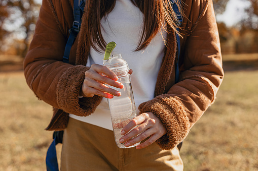 Female traveler with reusable plastic bottle of fresh water during hike in nature