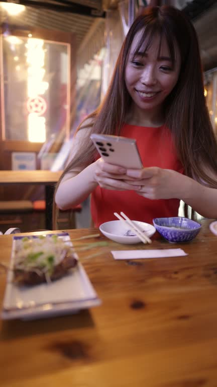 Business woman in orange dress taking photos of ‘Yakitori’ Japanese Chicken Skewers in Izakaya bar after work