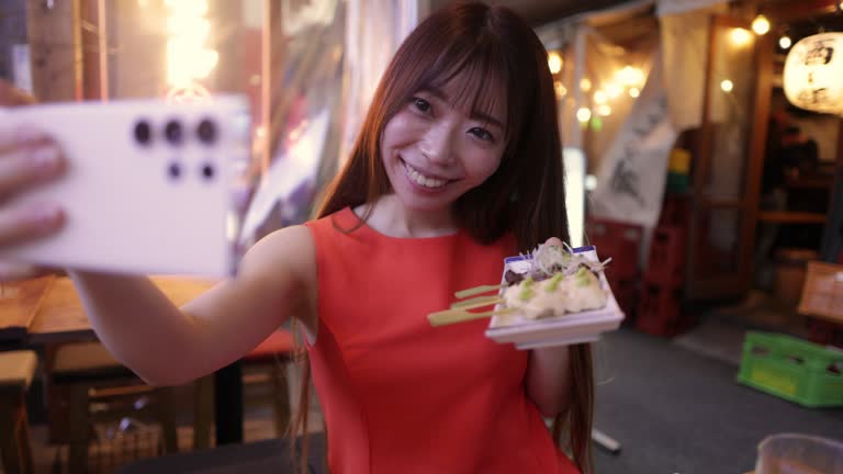 Business woman in orange dress taking photos of ‘Yakitori’ Japanese Chicken Skewers in Izakaya bar after work