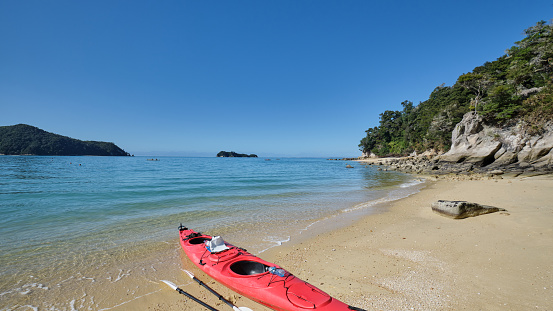 A kayak being laid at the shoreline on the beach. The place is one of the islands in Abel Tasman in New Zealand. It has clear water.