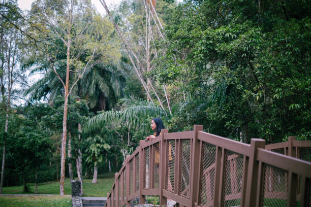 Asian woman with yellow jacket standing on bridge while looking at the river. Nature and wellbeing.