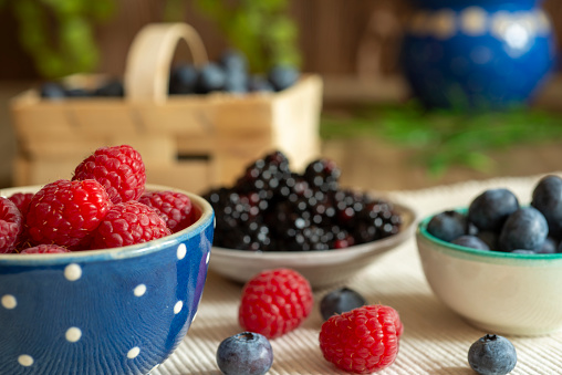 Rapsberries in blue bowl on a table with decoration with Blueberries and Blackberries