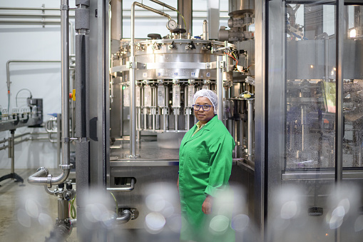 Female Operator looking at camera at an Automatic Liquid Filling Machine in Water Bottling Plant, Cape Town, South Africa