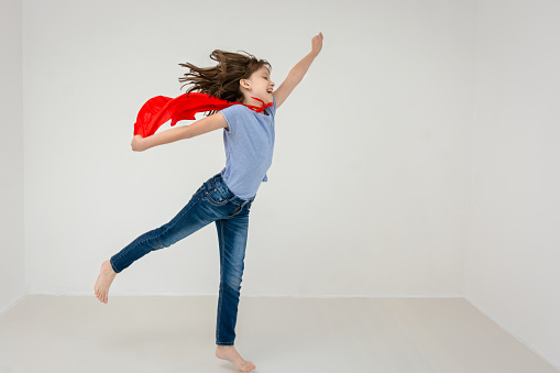 Girl in superhero costume jumping against white background