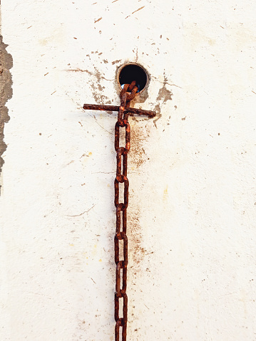 Old rusty chain sticking out of hole in uncorked cement wall. Architecture and construction details.
