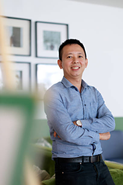 istock A portrait captures a young, confident Asian man standing with his arms folded and a bright smile on his face. He leans against a sofa, radiating positivity. 1500350865