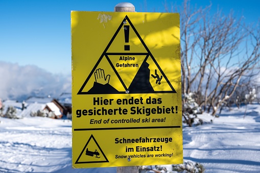 A yellow warning sign posted on the side of a snow-covered rocky mountain in Germany