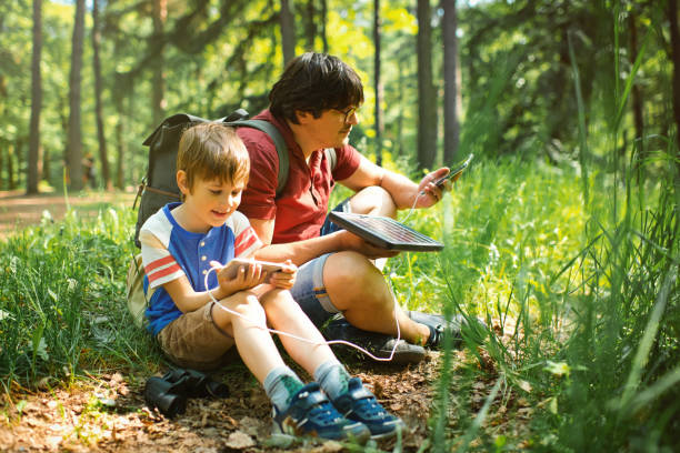 der kleine junge und sein vater verwenden tragbare solarbatterien, um smartphones in der natur aufzuladen. nachhaltiger lebensstil, ökologische alternative energien und ökologische konzepte. - energy fuel and power generation futuristic solar energy stock-fotos und bilder